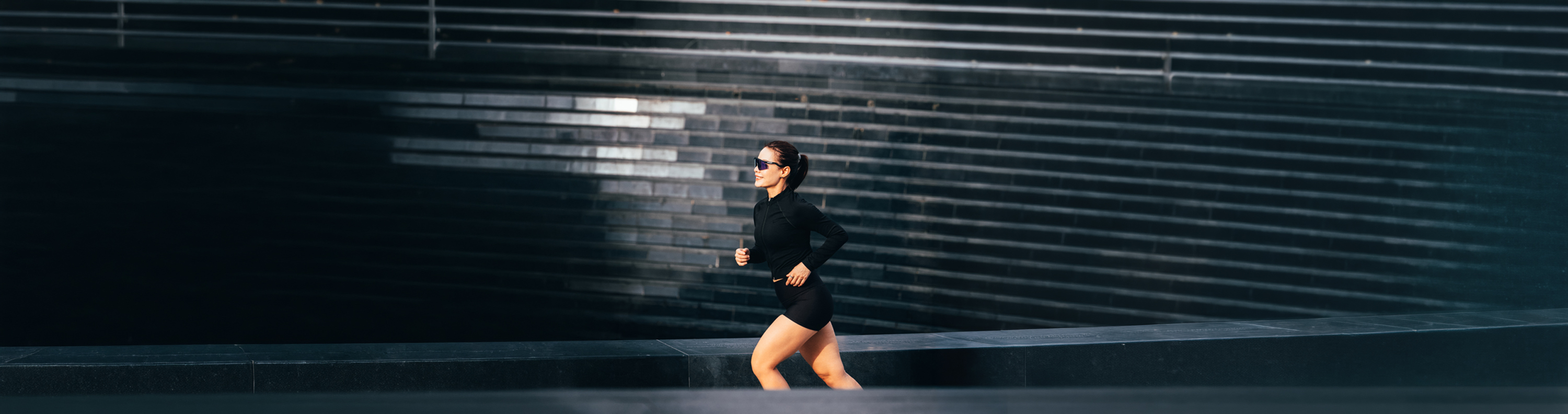 Runner in black sportswear striding past dark stadium steps at golden hour
